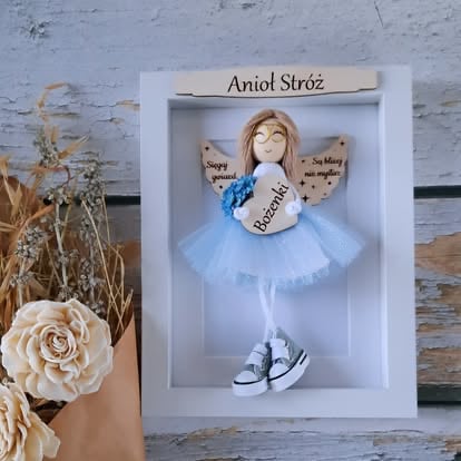 Ręcznie robiona drewniana laleczka anioł w białej ramce z jasnoniebieską tiulową spódniczką i trampkami, obok suszonych kwiatów